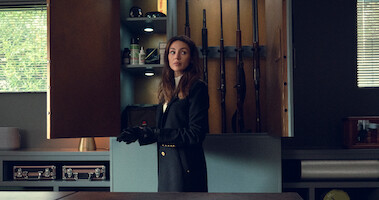 Michelle Keegan as Maya Stern stands in front of an open gun cabinet wearing black gloves in Season 1 of 'Fool Me Once'