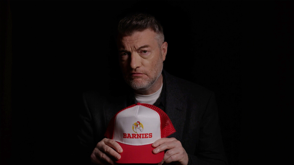 Charlie Brooker holds a hat that says "Barnies" 