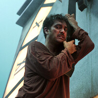 A man clings to the hand of a giant clock tower in an image from the series 'Joko Anwar’s Nightmares and Daydreams.'