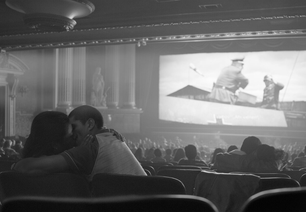Cena do filme 'Roma' mostra um casal de beijando nas cadeiras de um cinema, enquanto um filme passa na tela