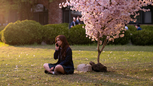 Anna Cathcart as Kitty Song Covey sits under a tree with pink blossoms in Season 2 of 'XO, Kitty' 