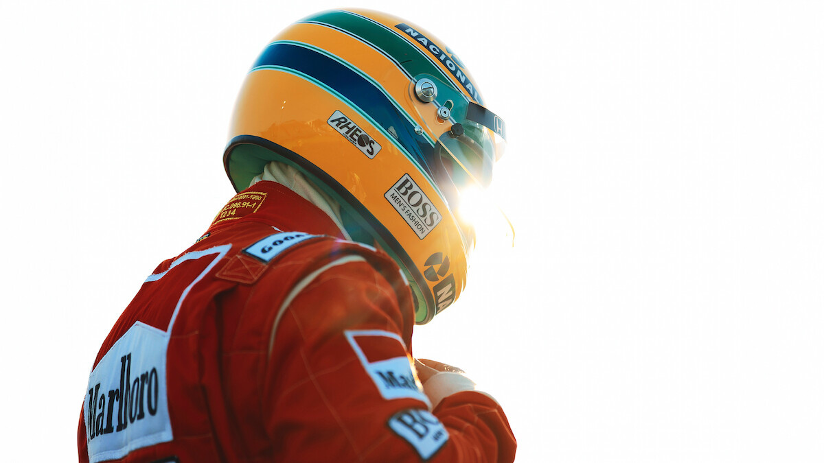 Ayrton Senna (Gabriel Leone) wears a red Marlboro jacket and a green-and-yellow helmet as he gears up to race.