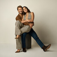 Adria Arjona sits on a Glen Powell's lap.