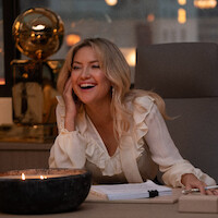 A temporada 1 de ‘A Dona da Bola’ traz Kate Hudson como Isla Gordon, que sorri rodeada por troféus de basquete em sua mesa de trabalho
