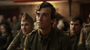 Young soldiers in vintage military uniforms sit closely together in a dimly lit indoor setting, focusing intently on something ahead, suggesting a wartime or historical atmosphere, possibly at a meeting or briefing.