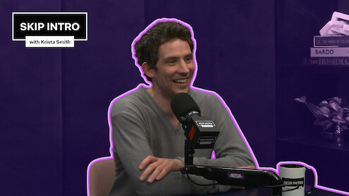 Josh O'Connor smiles while speaking into a podcast microphone in a purple studio, outlined with a neon accent, with a “Skip Intro with Krista Smith” graphic in the corner.