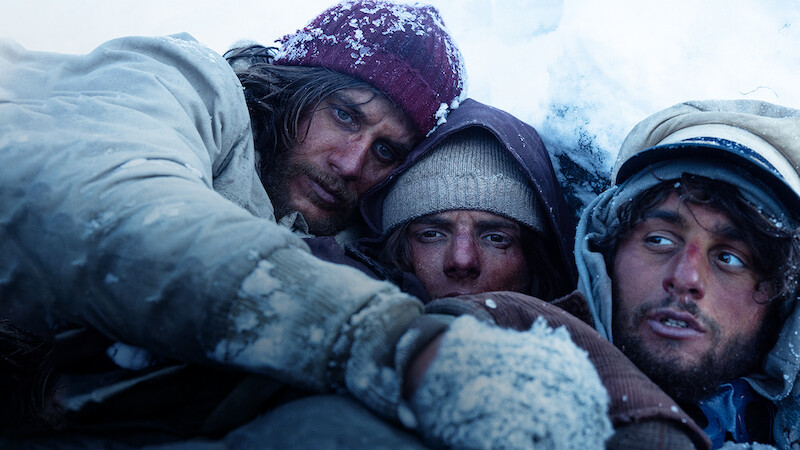A group of men huddle together for warmth in the snow in 'Society of the Snow'