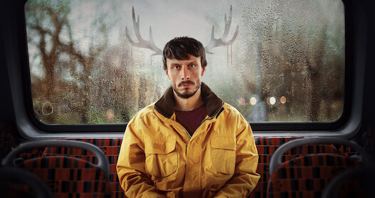 Richard Gadd as Donny Dunn sits in the back of a bus with reindeer antlers outside, behind his head in Season 1 of 'Baby Reindeer'