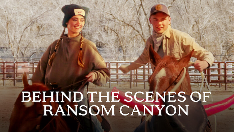 Da esquerda para a direita, Lizzy Greene e Garrett Wareing sorriem enquanto montam a cavalo em uma área cercada com árvores sem folhas. O texto na parte inferior diz “BASTIDORES DE RANSOM CANYON”.