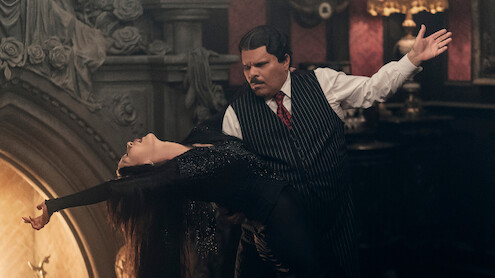Catherine Zeta-Jones, como Mortícia Addams, e Luis Guzmán, como Gomez Addams, dançam juntos em frente a uma lareira na temporada 2 de ‘Wandinha’.