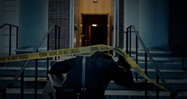A police officer pulls up crime scene tape.