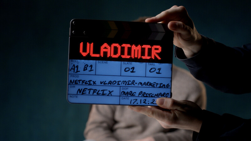 Clapperboard with "VLADIMIR" illuminated, held in front of a blurred person on a dark set, showing film production details for a Netflix project.