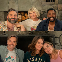 Six adults sitting closely together in front of a stone fireplace, smiling warmly in a cozy living room setting, wearing casual clothes, suggesting a relaxed and friendly gathering indoors.