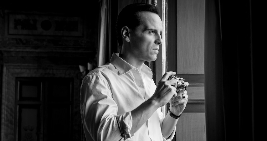 Black and white photo of Andrew Scott as Tom Ripley holding a camera while looking out of a window in Season 1 of 'Ripley'