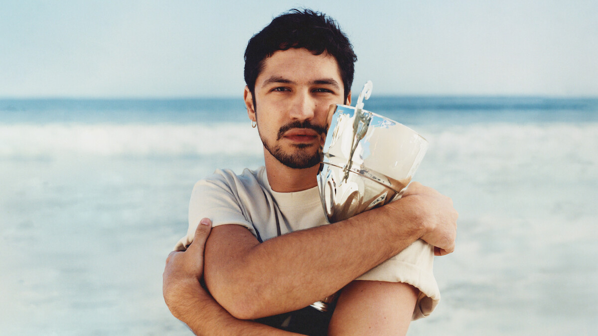 Gabriel Leone wears a white t-shirt and clutches a trophy to his chest.