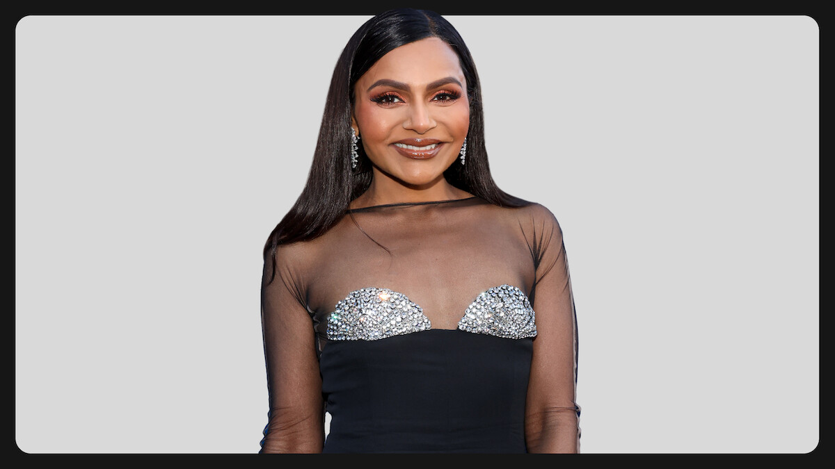 Woman wearing a black dress with sheer top and sparkling embellishments, standing in front of a light gray background, smiling and posing for the camera, formal event setting.