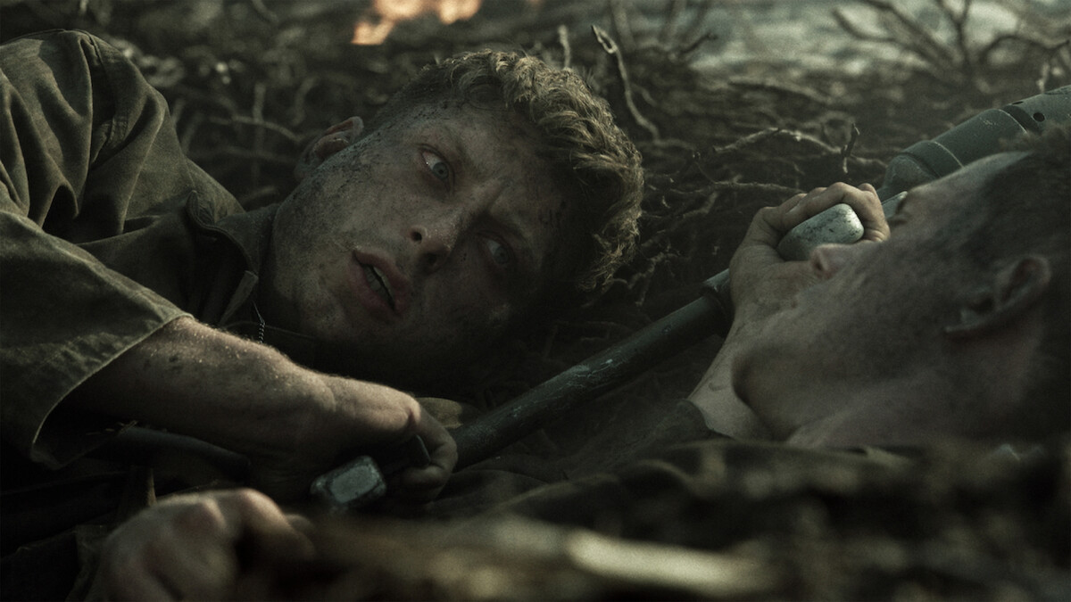 Two soldiers lying close together in a muddy, war-torn trench, covered in dirt and looking tense and exhausted, surrounded by twisted roots and debris during battle.