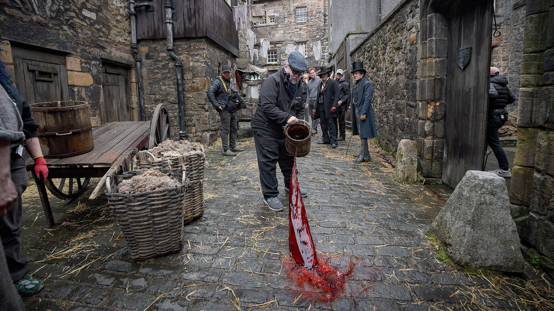 Guillermo del Toro throws a bucket of blood into cobblestoned streets on the set of Frankenstein.