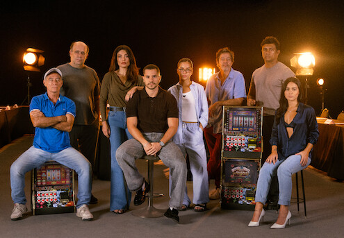 Elenco principal da série "Donos do Jogo" posa ao lado de máquinas caça-níquel