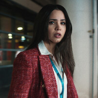 Sofia Carson com uma expressão aflita usando um blazer vermelho.