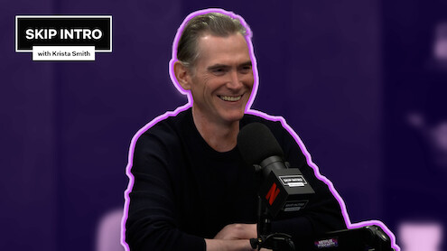 Billy Crudup sits smiling in front of a microphone during a podcast recording for "Skip Intro with Krista Smith." The background is purple, and the podcast logo appears in the top left corner.