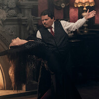 Catherine Zeta-Jones, como Mortícia Addams, e Luis Guzmán, como Gomez Addams, dançam juntos em frente a uma lareira na temporada 2 de ‘Wandinha’.