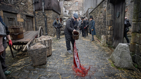 Guillermo del Toro throws a bucket of blood into cobblestoned streets on the set of Frankenstein.