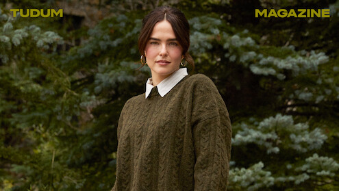 Zoey Deutch stands against a backdrop of trees