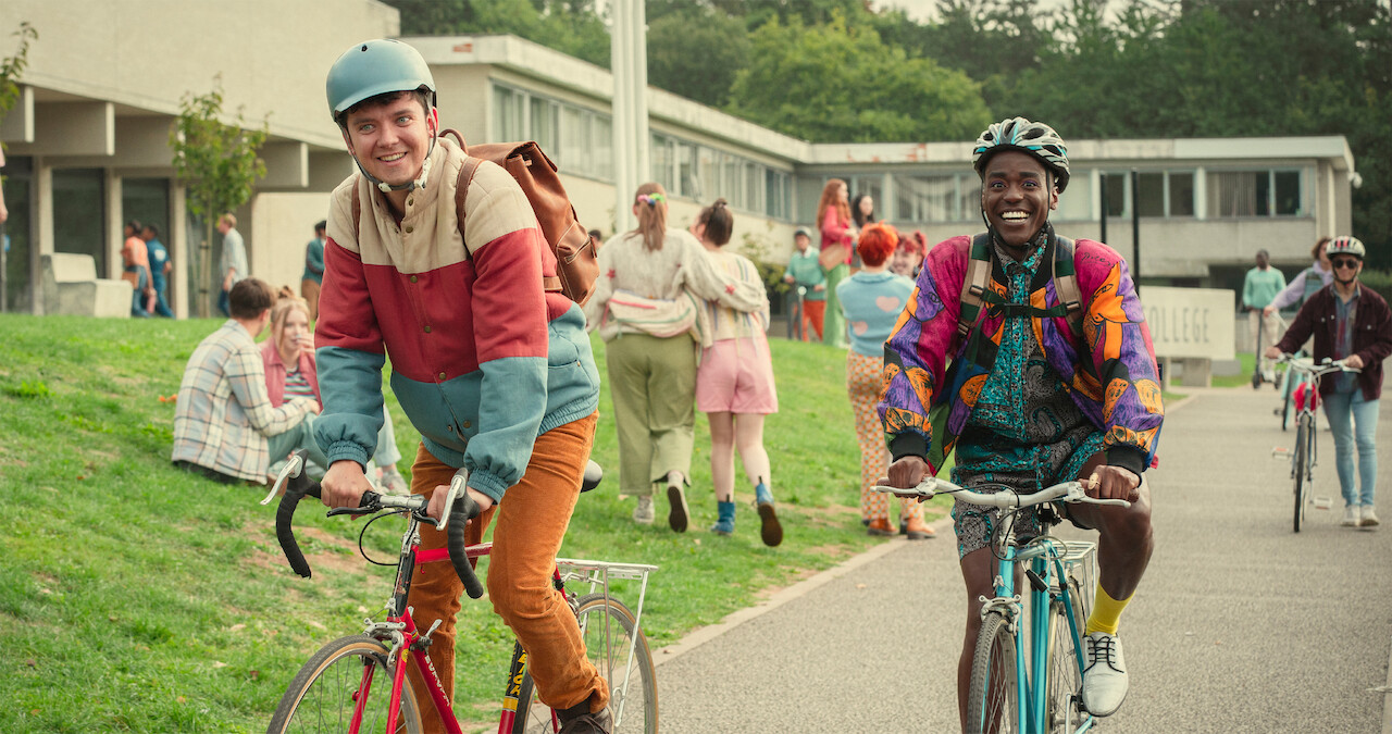 Asa Butterfield as Otis and Ncuti Gatwa as Eric ride their bikes to school in Season 4 of 'Sex Education.'