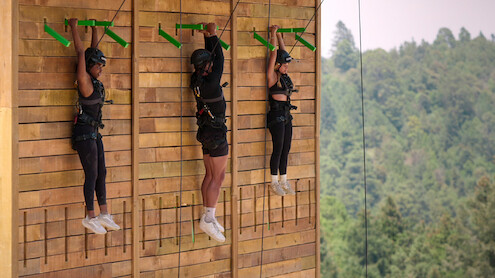 Quori-Tyler Bullock, Chase DeMoor, and Georgia Hassarati hanging from a climbing wall during a challenge
