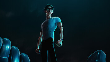 Ken Sato (Christopher Sean) wears a tight gray T-shirt and stands against a black background.