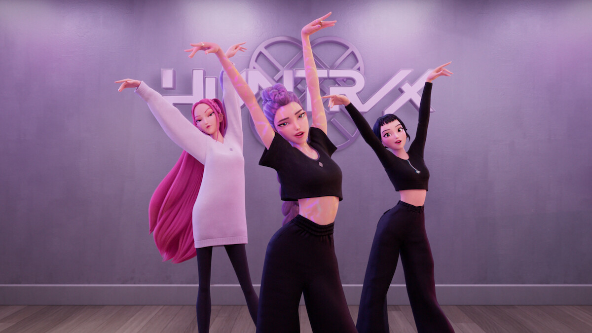 Three animated women in a modern dance studio pose gracefully with raised arms, wearing stylish black and pink outfits, wooden floor, and a wall with the "HUNTR/X" sign in the background.
