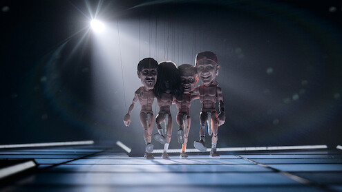 The Red Hot Chili Peppers as marionettes on strings walk across the stage with buff plastic doll bodies exposed to the elements, just the signature sock covering their goods.
