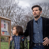 A concerned man with a beard stands outdoors with a young child, both looking in the same direction. Behind them is a wooden bulletin board with "Have you seen me?" posters. Leafless trees and cloudy sky suggest winter or early spring.