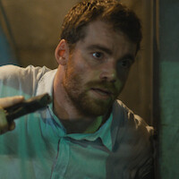 Gabriel Basso, como Peter Sutherland, se apoia em uma parece enquanto segura uma arma na temporada 2 de ‘O Agente Noturno’.