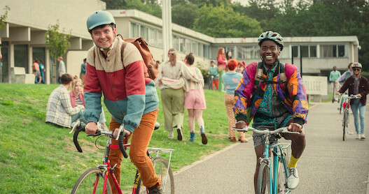 Asa Butterfield as Otis and Ncuti Gatwa as Eric ride their bikes to school in Season 4 of 'Sex Education.'