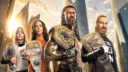 Four wrestling champions stand in a modern city with skyscrapers and a sunset sky, each holding championship belts, appearing strong and confident.