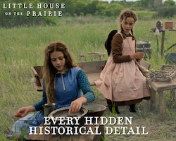 Two girls in prairie dresses sit outdoors beside rustic wooden tables and vintage cooking tools in a grassy field, reenacting a historical pioneer camp scene. A campfire is visible in the foreground, trees in the background.
