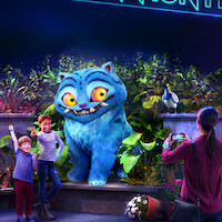A large, animated blue cat with yellow eyes poses with two happy children in front of lush, glowing plants, while an adult takes their photo in a colorful, vibrant nighttime setting.