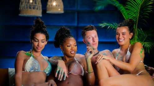 Cast members of 'Temptation Island' in swimsuits covered in body paint sit together on a couch.