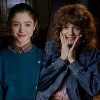 A split-image of Natalia Dyer at two different ages: younger on the left, sitting in a vintage-style room and smiling calmly; older on the right, in a softly lit modern setting, wearing a denim jacket and expressing excitement.