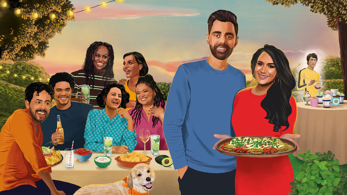 A group of people enjoying an outdoor dinner party with drinks and food, set in a garden with string lights. A couple stands in the front holding a large dish, while a dog sits beside them and more food is on a table in the background.