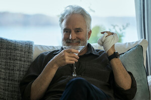 Bradley Whitford as Todd Penn in 'The Diplomat,' holds a martini glass in one hand and smiles while his other hand is wrapped in a cloth bandage.