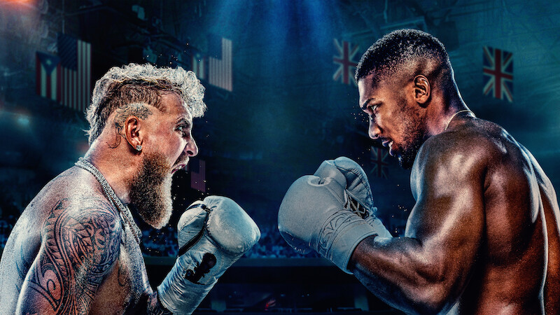 Jake Paul and Anthony Joshua face off shirtless in a dramatic, intense promotional poster with their country flags in the background