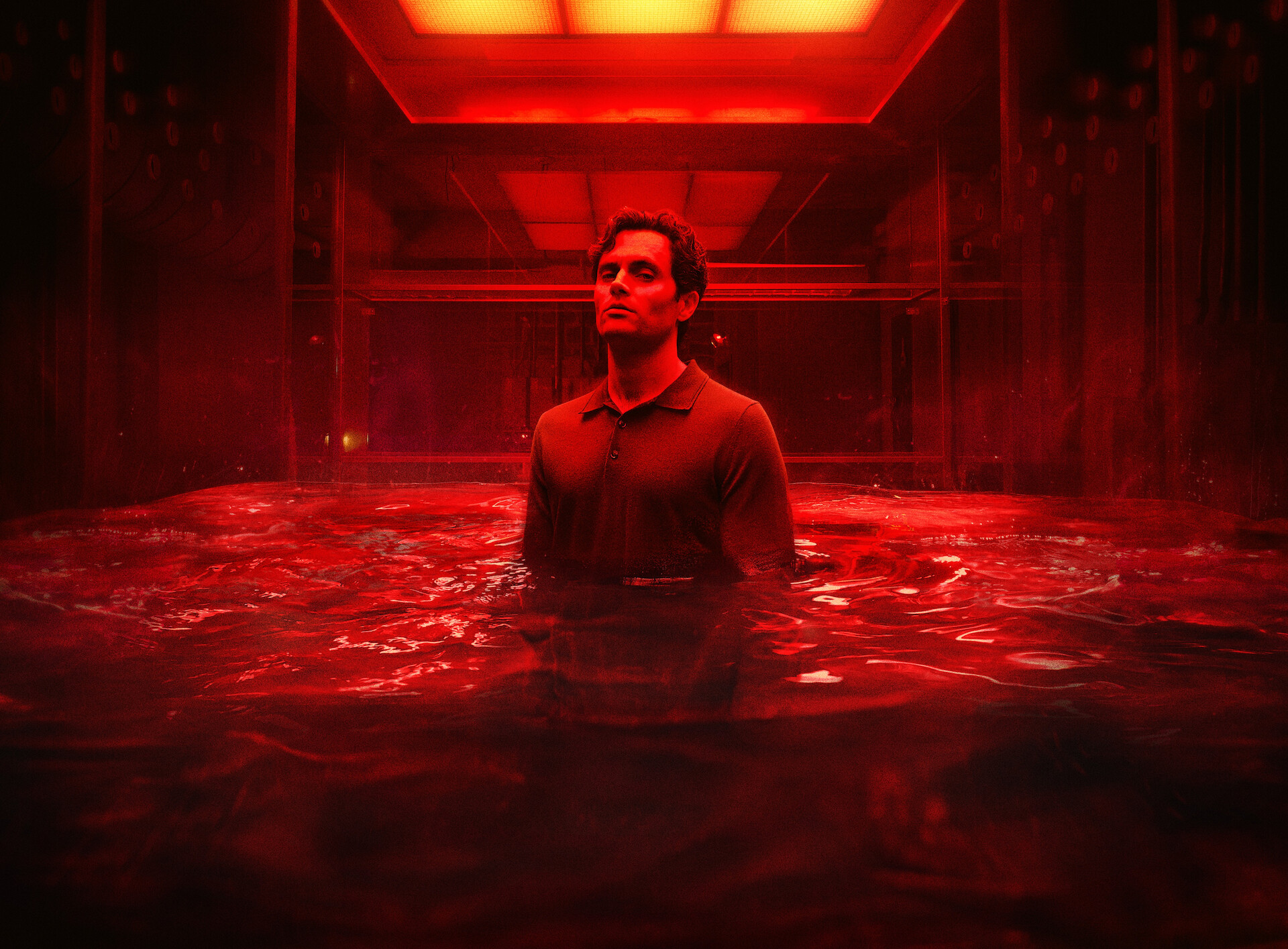 You key art - Joe standing in a room chest deep in water, illuminated by a red light. 