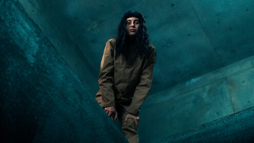 Milena Smit wearing a khaki uniform looks through a hole in the floor in an image from the film 'The Platform 2.'