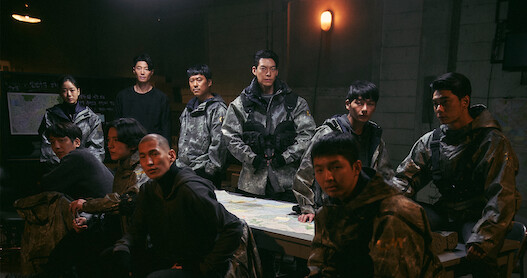 Several people wearing futuristic tactical gear gather around a table.