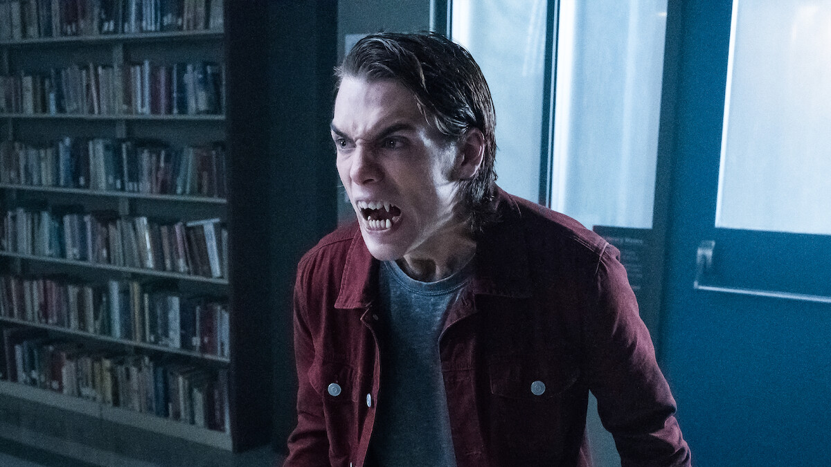A person with werewolf features crouches on a dark roof at night, wearing a striped shirt and hoodie, with glowing eyes, sharp teeth, and aggressive expression in a dramatic, suspenseful setting.