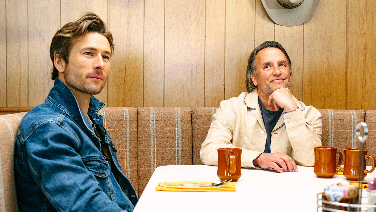 Glen Powell and Richard Linklater sit at a restaurant booth together.