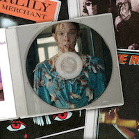 Uma caixa de CD com a foto de uma jovem de vestido florido, coberta de sangue, em um quarto pouco iluminado. O CD está sobre diversas capas de álbuns musicais com cores vibrantes e artes gráficas.
